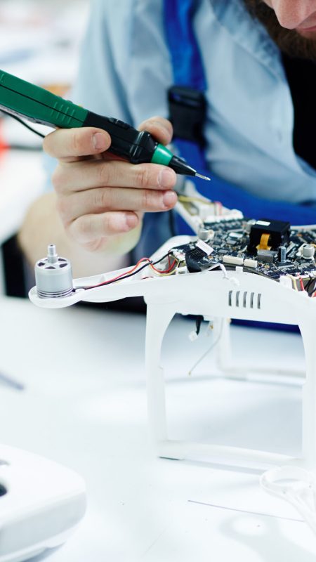 Closeup shot of unrecognizable man  testing electric current in circuit board of disassembled drone using multimeter tool on table in maintenance shop