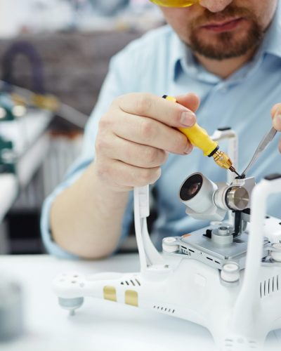 Closeup shot of man working on assembling new surveillance system using quadcopter drone with  action camera on table with different tools in modern workshop