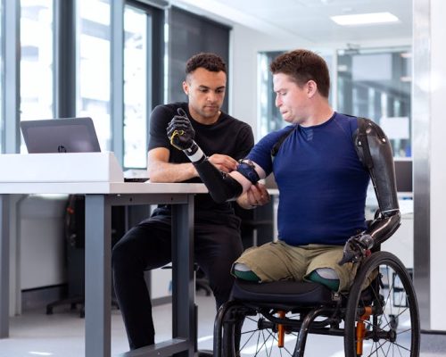 Engineer adjusts prosthetic arm for seated man in wheelchair, focusing on modern technology in healthcare.
